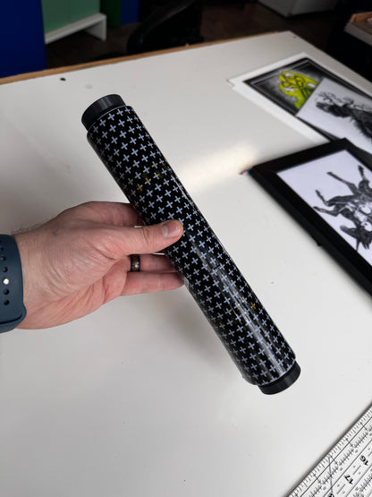 Hand holding a roll of tattoo bandage above a white surface with framed pictures in the background.