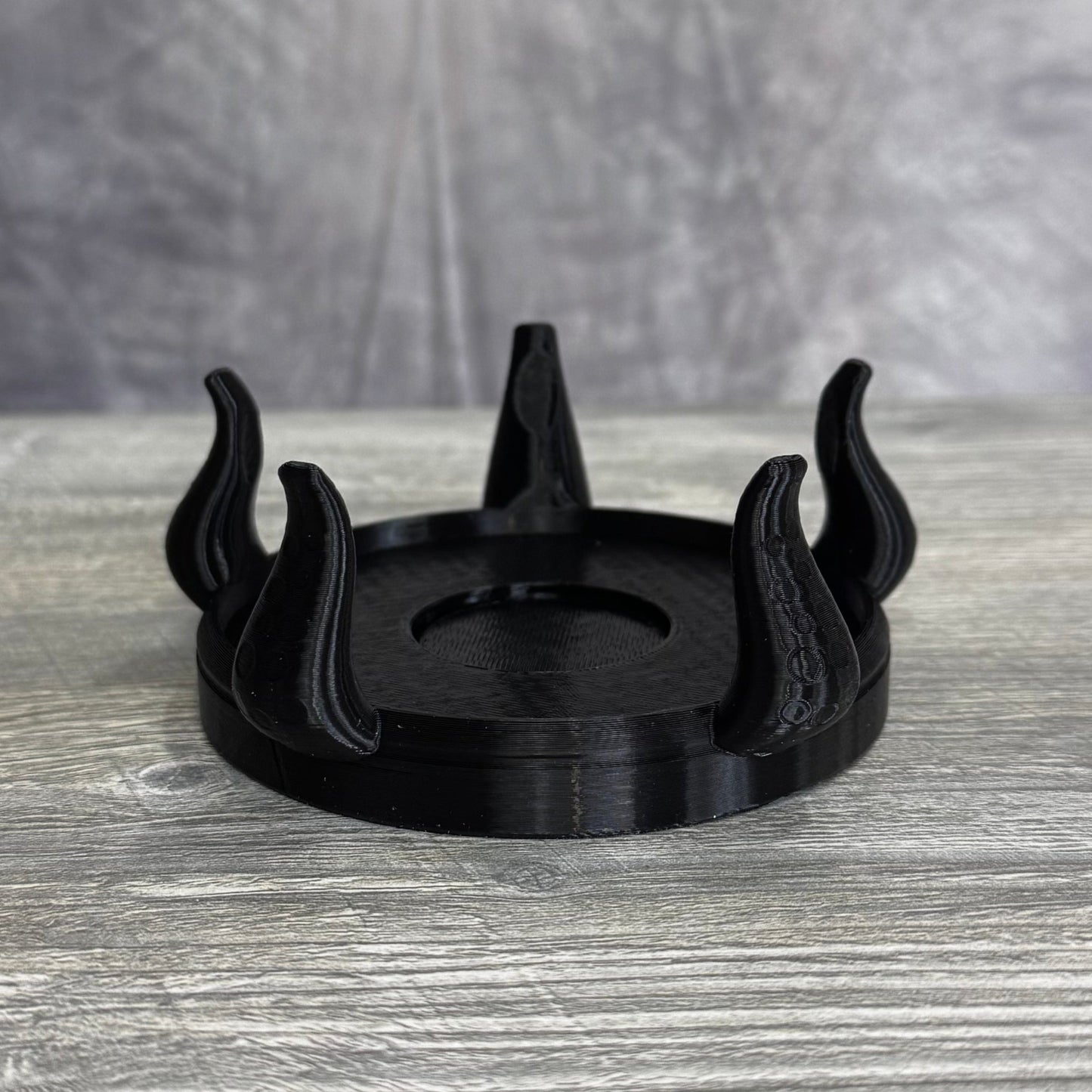 Black plastic base with five tentacles, sitting gray wood table.