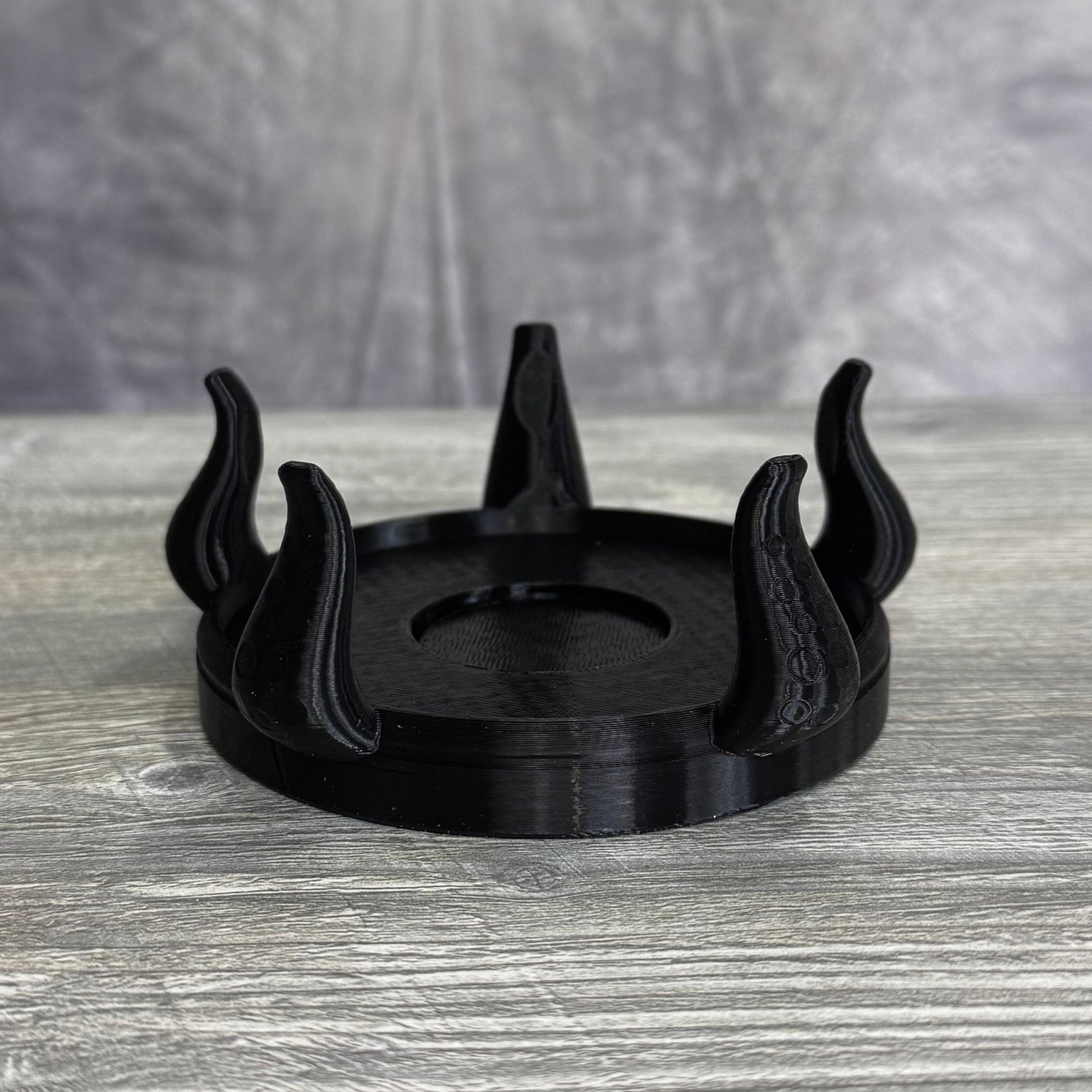 Black plastic base with five tentacles, sitting gray wood table.
