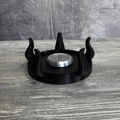 Black plastic base with five tentacles, with silver plastic disc on top, sitting gray wood table.