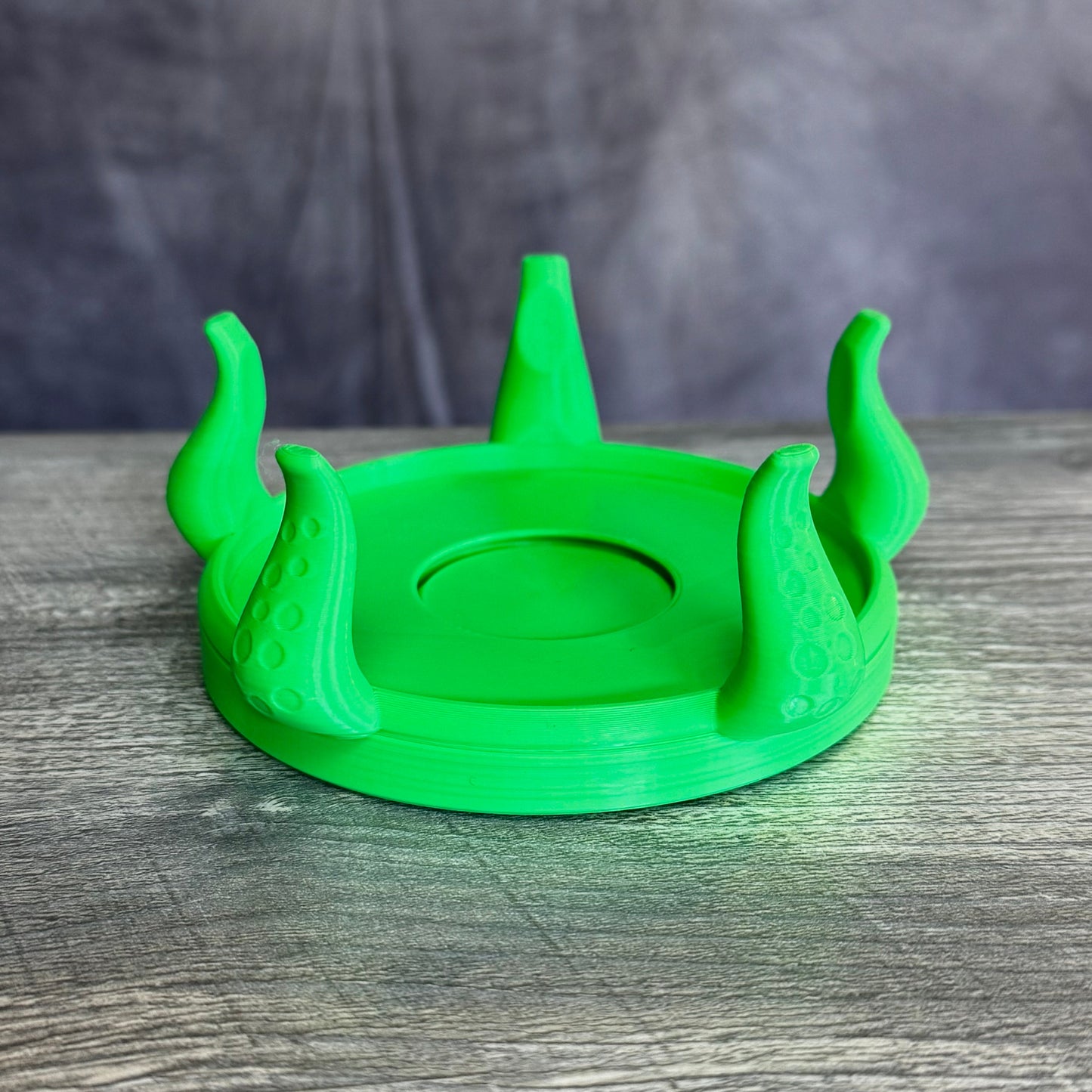 Green plastic base with five tentacles, sitting gray wood table.